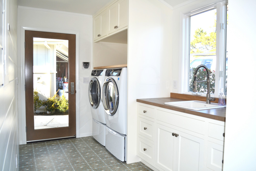 他の地域にある高級な中くらいなカントリー風のおしゃれな家事室 (ll型、ドロップインシンク、落し込みパネル扉のキャビネット、白いキャビネット、木材カウンター、茶色いキッチンパネル、木材のキッチンパネル、白い壁、テラコッタタイルの床、左右配置の洗濯機・乾燥機、マルチカラーの床、茶色いキッチンカウンター、塗装板張りの壁) の写真