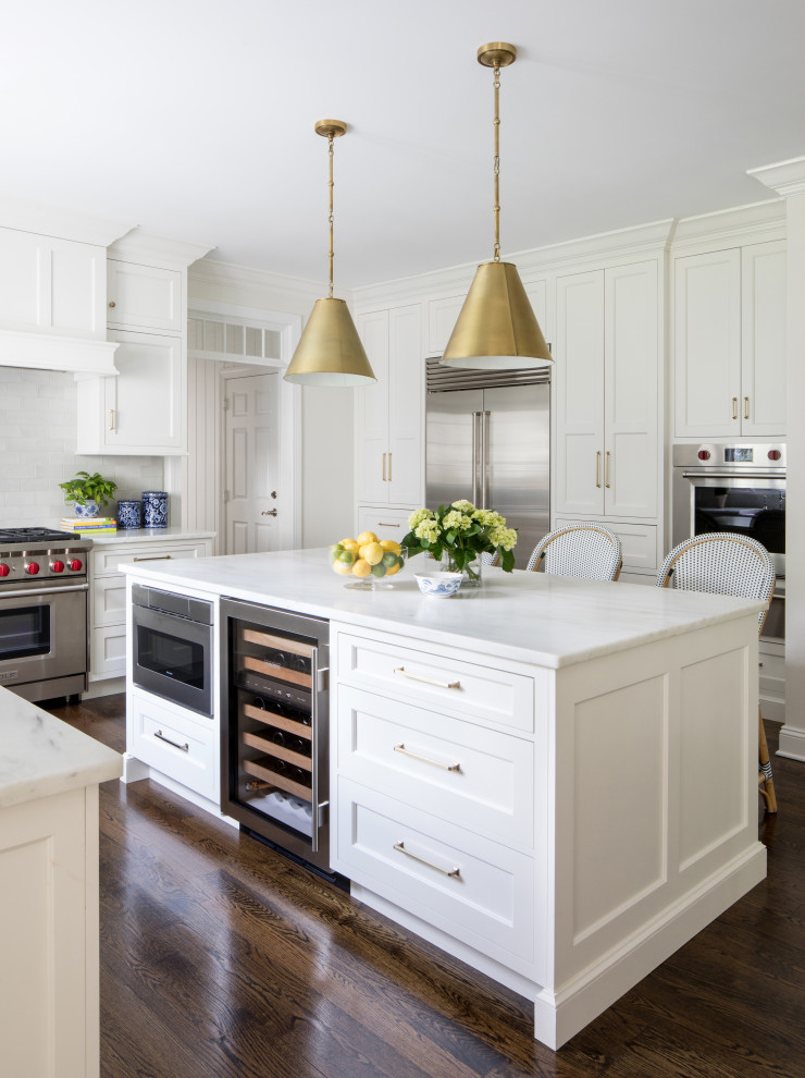 Inspiration for a traditional u-shaped kitchen in New York with shaker cabinets, white cabinets, white splashback, stainless steel appliances, dark hardwood floors, with island, brown floor and white benchtop.