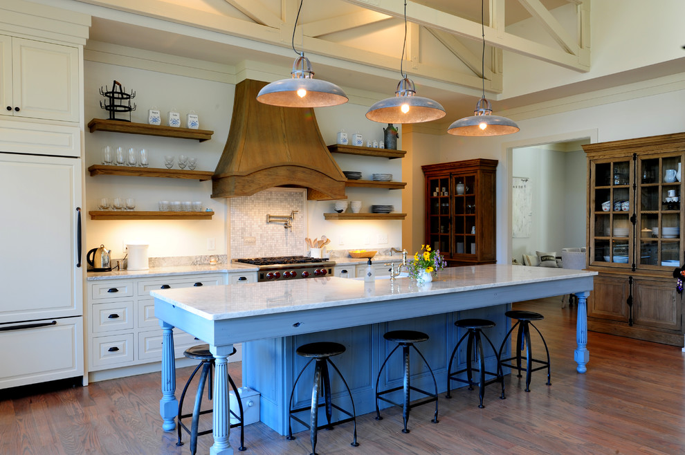 Mid-sized arts and crafts galley medium tone wood floor open concept kitchen photo with a farmhouse sink, raised-panel cabinets, beige cabinets, marble countertops, gray backsplash, stone tile backsplash, stainless steel appliances and an island
