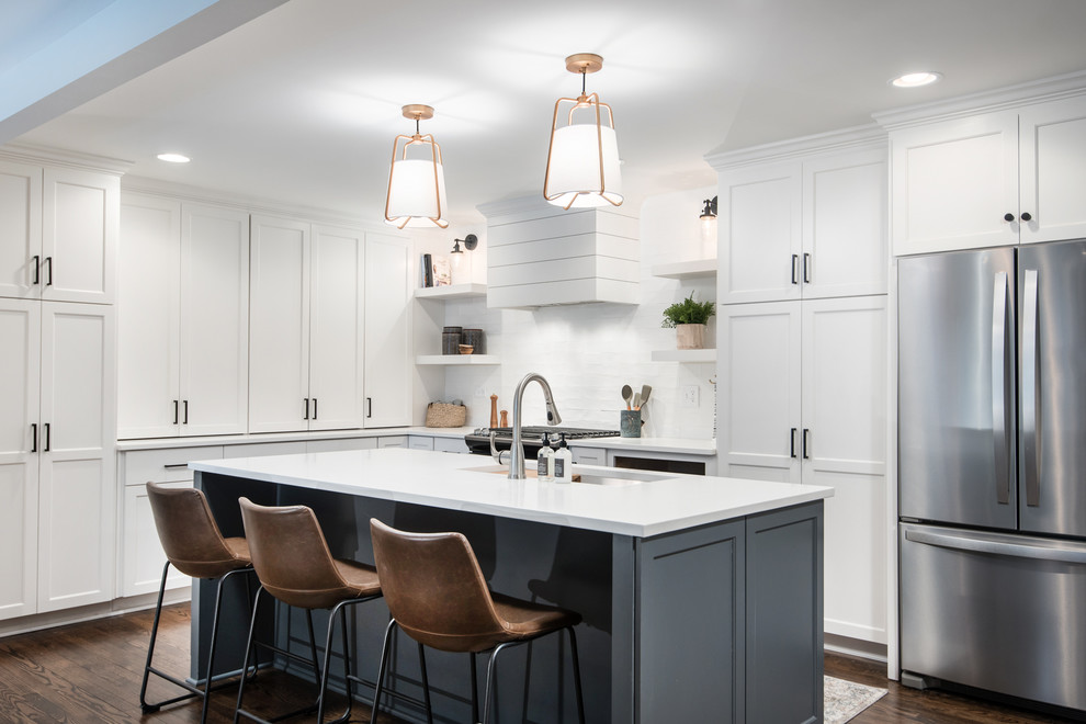 This is an example of a transitional l-shaped kitchen in Chicago with an undermount sink, shaker cabinets, white cabinets, white splashback, stainless steel appliances, dark hardwood floors, with island, brown floor and white benchtop.