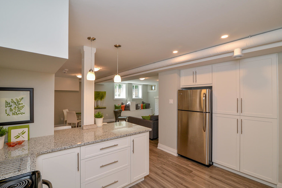 Example of a mid-sized transitional u-shaped medium tone wood floor and gray floor open concept kitchen design with an undermount sink, shaker cabinets, white cabinets, granite countertops, stainless steel appliances and a peninsula