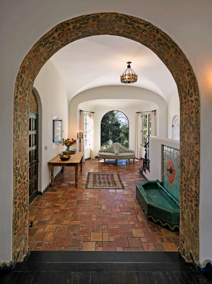 This is an example of an expansive mediterranean foyer in Los Angeles with white walls, terra-cotta floors and a single front door.
