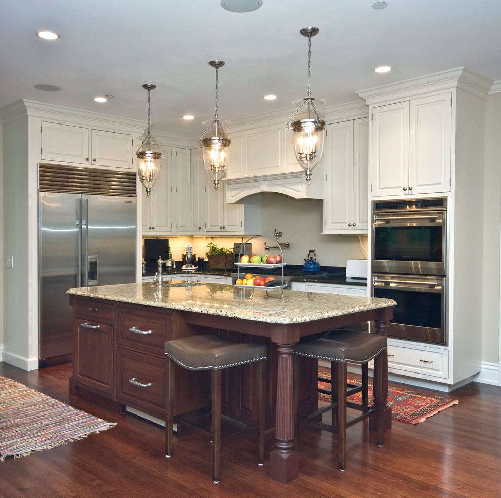 Mid-sized traditional l-shaped open plan kitchen in Chicago with raised-panel cabinets, white cabinets, granite benchtops, beige splashback, stainless steel appliances, dark hardwood floors, with island and a double-bowl sink.