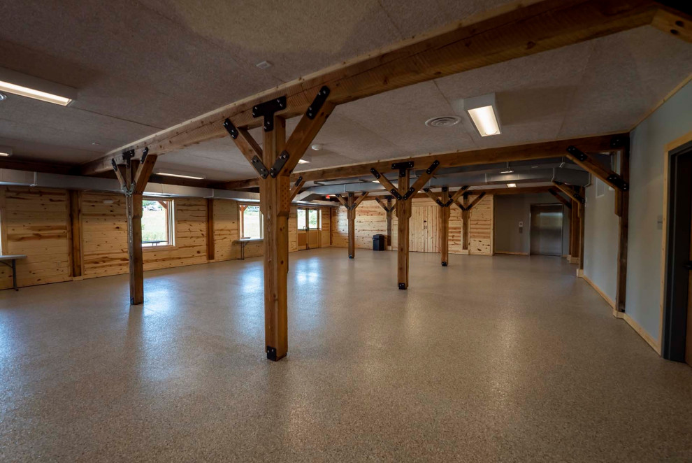 This is an example of a large rustic walk-out basement with no fireplace, grey floors, exposed beams and wood walls.