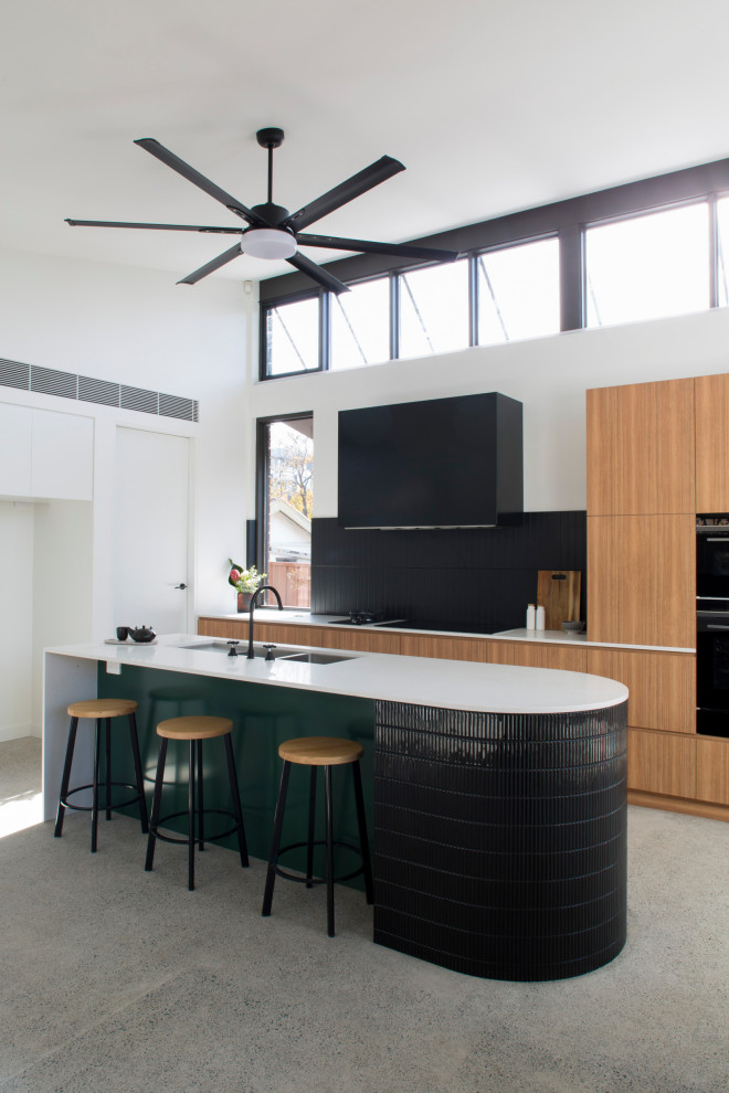 Mid-sized contemporary open plan kitchen in Sydney with recessed-panel cabinets, light wood cabinets, marble benchtops, black splashback, ceramic splashback, black appliances, with island, white benchtop, a double-bowl sink, concrete floors and grey floor.