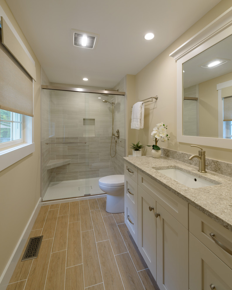Photo of a transitional 3/4 bathroom in Boston with shaker cabinets, grey cabinets, an alcove shower, a two-piece toilet, gray tile, ceramic tile, grey walls, ceramic floors, an undermount sink, granite benchtops, grey floor and a sliding shower screen.