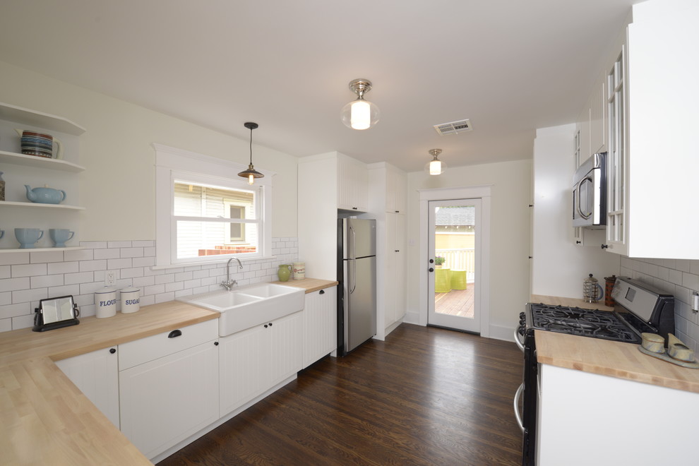 Photo of a mid-sized arts and crafts u-shaped eat-in kitchen in Los Angeles with a peninsula, beaded inset cabinets, white cabinets, wood benchtops, white splashback, subway tile splashback, stainless steel appliances, a farmhouse sink and dark hardwood floors.