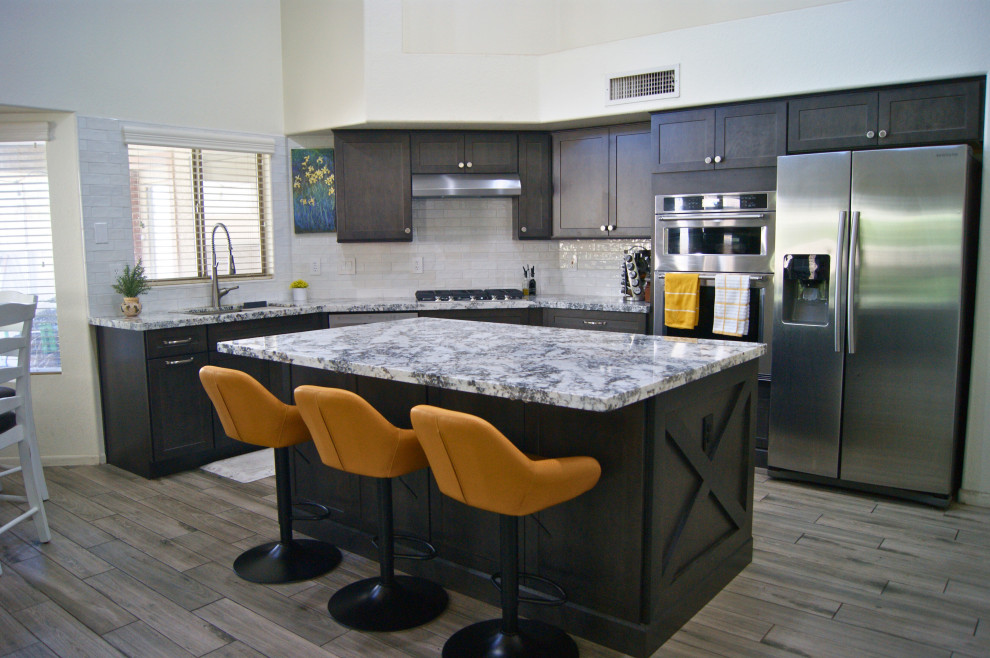 Inspiration for a mid-sized modern l-shaped porcelain tile and gray floor open concept kitchen remodel in Phoenix with an undermount sink, shaker cabinets, brown cabinets, granite countertops, white backsplash, subway tile backsplash, stainless steel appliances, an island and white countertops