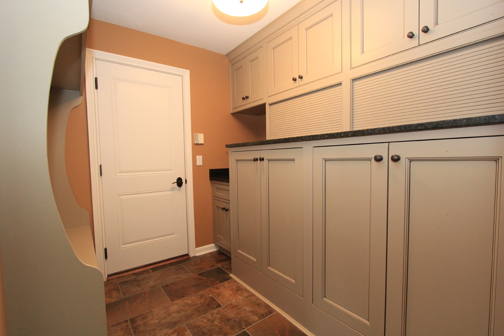 This is an example of a mid-sized transitional galley utility room in Cincinnati with an undermount sink, granite benchtops, ceramic floors, a concealed washer and dryer, recessed-panel cabinets and brown walls.