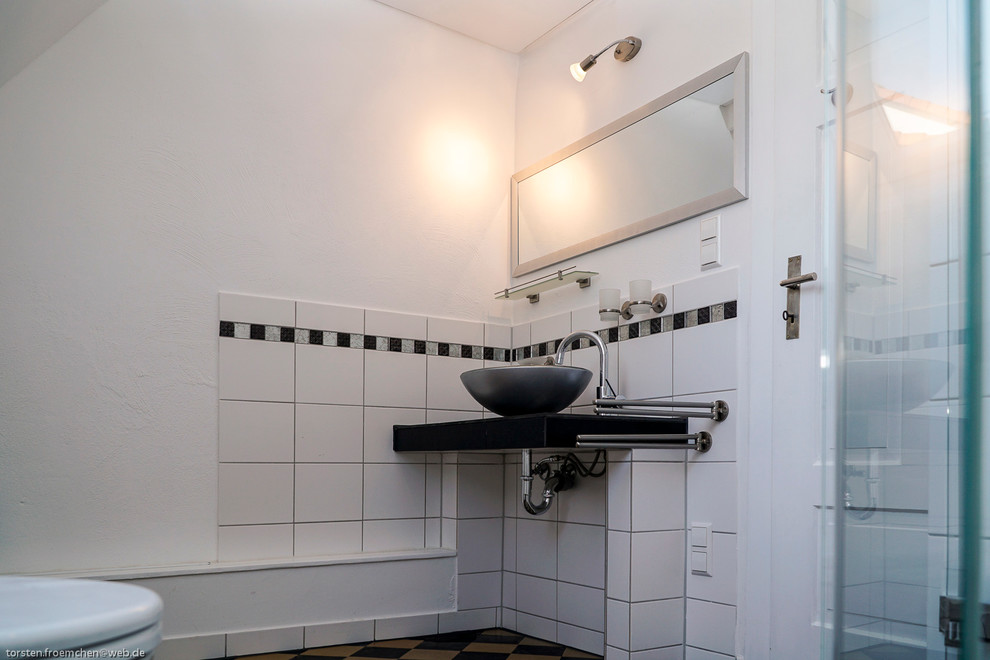 This is an example of a small country 3/4 bathroom in Berlin with a corner shower, a two-piece toilet, black and white tile, cement tile, white walls, concrete floors, a vessel sink and glass benchtops.
