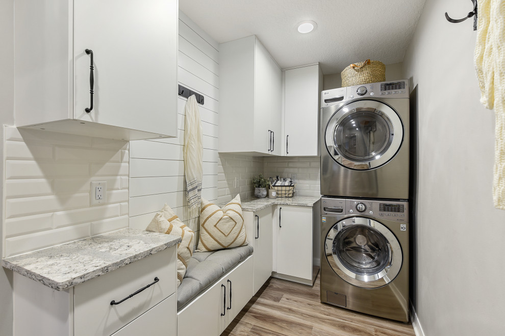 This is an example of a country l-shaped utility room in Jacksonville with flat-panel cabinets, white cabinets, grey walls, medium hardwood floors, a stacked washer and dryer, brown floor and grey benchtop.