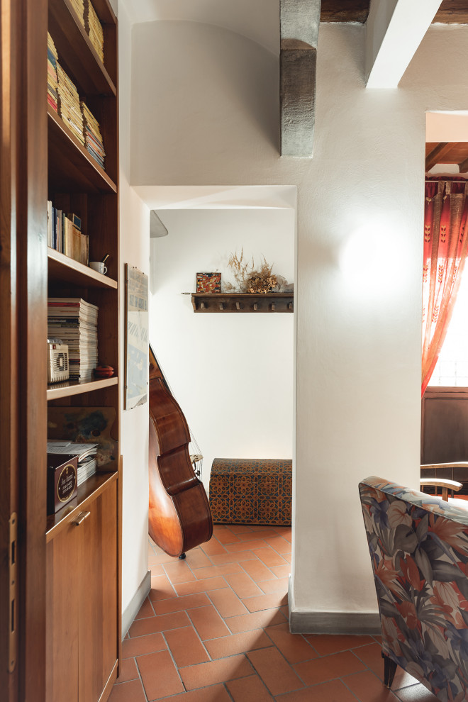 Imagen de biblioteca en casa abierta moderna pequeña con paredes blancas, suelo de baldosas de terracota, televisor independiente, suelo rojo y vigas vistas