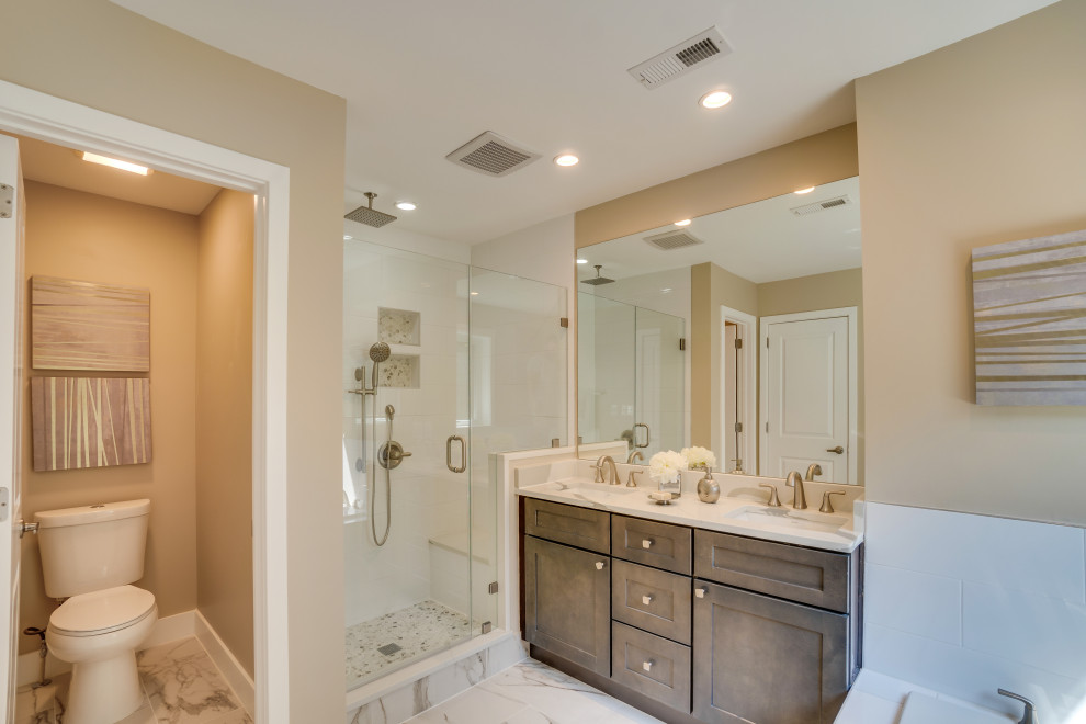 Photo of a large arts and crafts master bathroom in DC Metro with raised-panel cabinets, brown cabinets, a drop-in tub, a shower/bathtub combo, a one-piece toilet, white tile, ceramic tile, beige walls, ceramic floors, a drop-in sink, granite benchtops, white floor, a hinged shower door, white benchtops, an enclosed toilet, a double vanity and a built-in vanity.