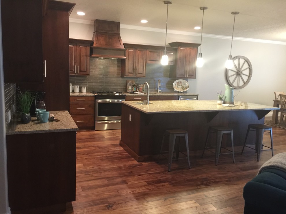 Mid-sized mountain style l-shaped dark wood floor open concept kitchen photo in Boise with an undermount sink, raised-panel cabinets, dark wood cabinets, granite countertops, gray backsplash, glass tile backsplash, stainless steel appliances and an island