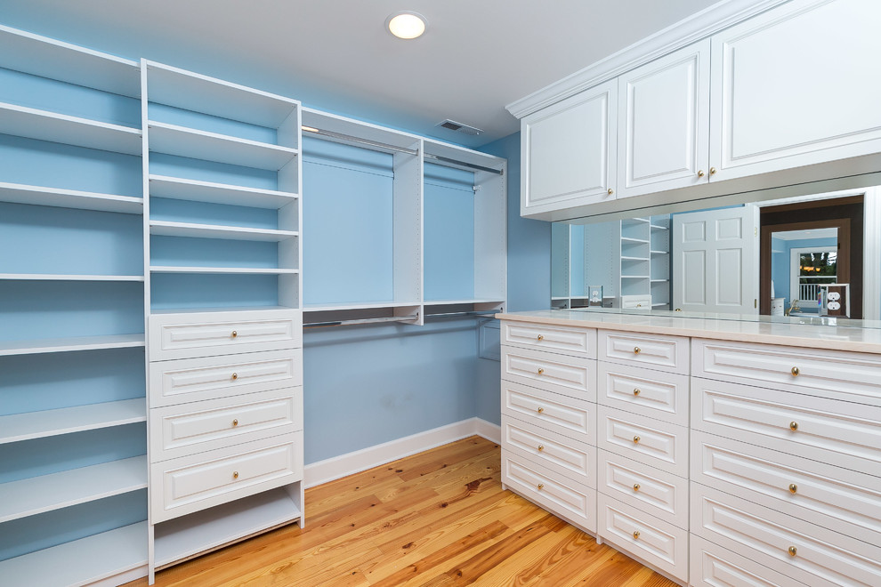 Large transitional gender-neutral dressing room in Baltimore with white cabinets, medium hardwood floors and raised-panel cabinets.