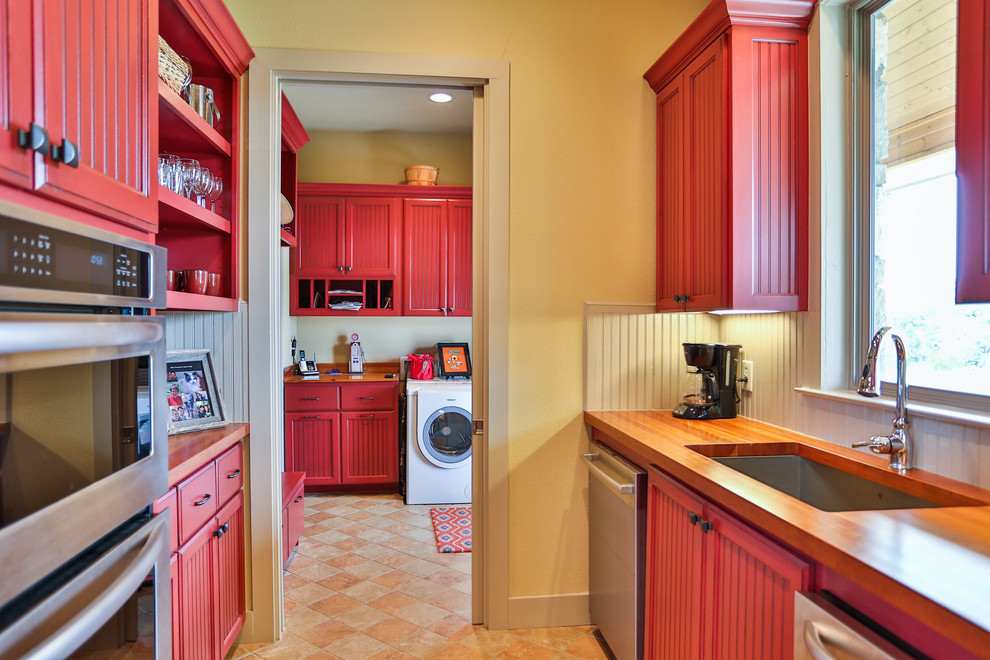This is an example of a mid-sized country galley kitchen in Austin with an undermount sink, red cabinets, wood benchtops, yellow splashback, timber splashback, stainless steel appliances, ceramic floors and recessed-panel cabinets.