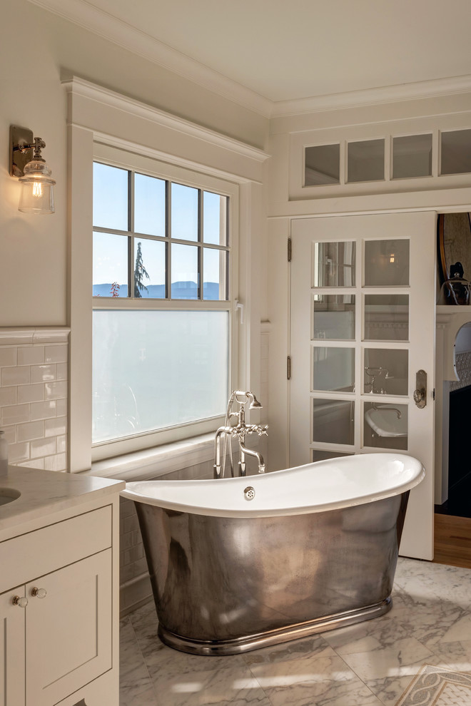 This is an example of a beach style master bathroom in Seattle with shaker cabinets, white cabinets, a freestanding tub, white tile, subway tile, white walls, an undermount sink and grey floor.