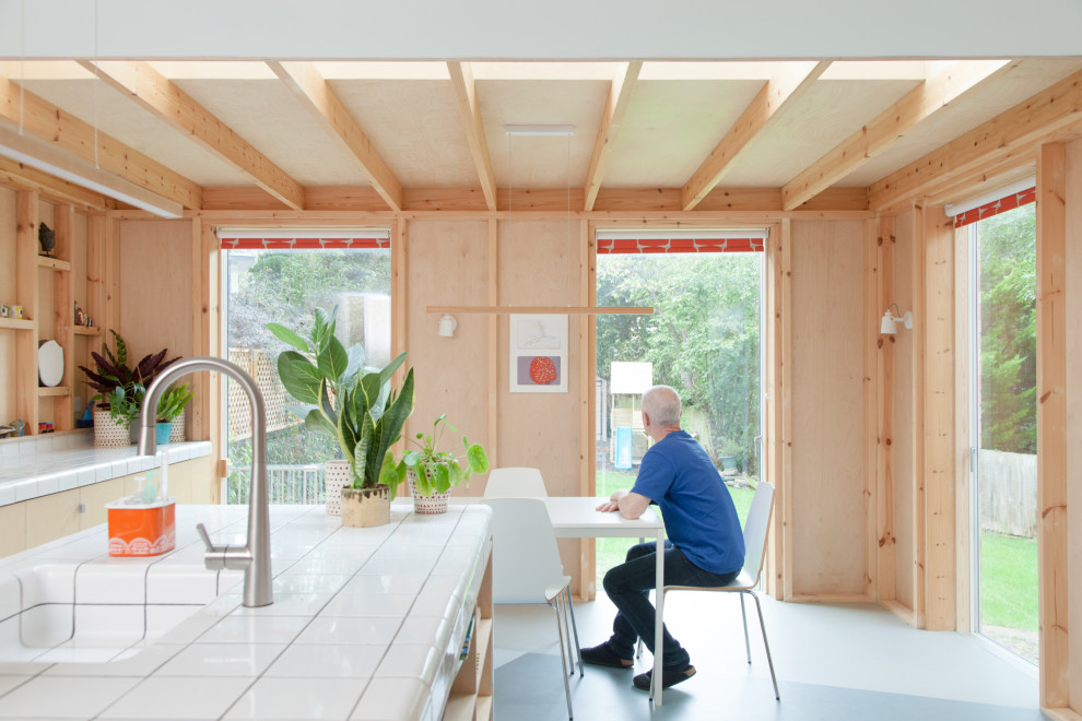 Foto på ett mellanstort funkis vit kök med öppen planlösning, med en integrerad diskho, släta luckor, skåp i ljust trä, kaklad bänkskiva, linoleumgolv, en köksö och grått golv