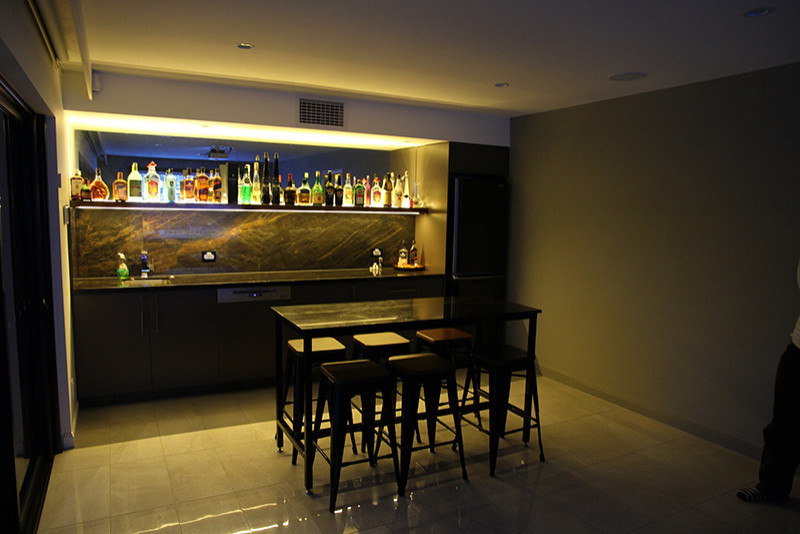 This is an example of a mid-sized modern single-wall wet bar in Brisbane with an undermount sink, beaded inset cabinets, grey cabinets, quartz benchtops, black splashback, ceramic splashback, ceramic floors, white floor and black benchtop.