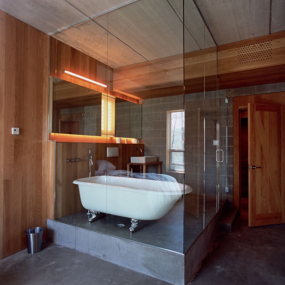 Large industrial bathroom in New York with a console sink, furniture-like cabinets, light wood cabinets, concrete benchtops, a claw-foot tub, an open shower, a wall-mount toilet, gray tile, cement tile, grey walls and concrete floors.