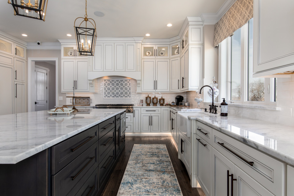 This is an example of a transitional l-shaped eat-in kitchen in Philadelphia with a farmhouse sink, recessed-panel cabinets, white cabinets, stainless steel appliances, dark hardwood floors, with island, brown floor, white benchtop, quartz benchtops, white splashback and porcelain splashback.