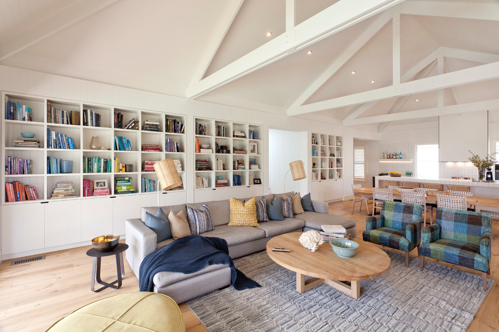 This is an example of a beach style open concept living room in Melbourne with a library, white walls, medium hardwood floors, no fireplace, no tv and brown floor.