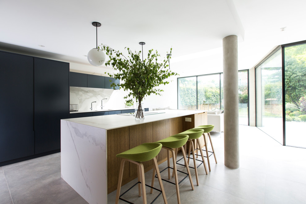 This is an example of an expansive modern galley open plan kitchen in London with flat-panel cabinets, black cabinets, marble benchtops, white splashback, marble splashback, concrete floors, with island, grey floor, an undermount sink and white benchtop.