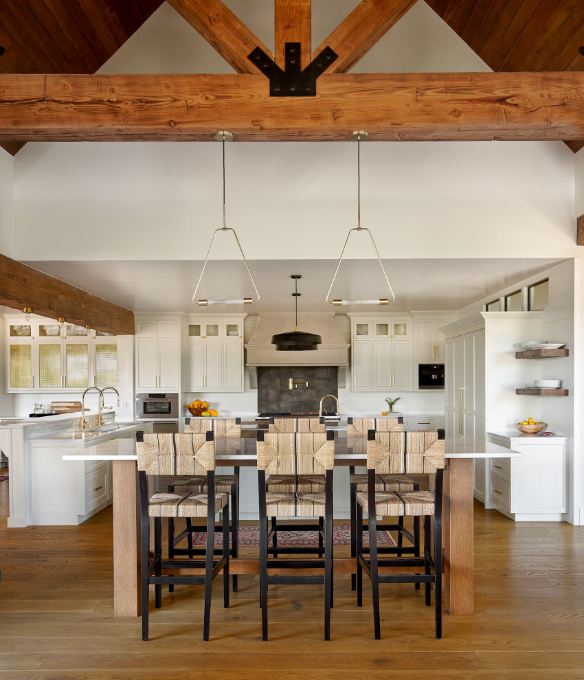 Expansive rural l-shaped open plan kitchen in Denver with a submerged sink, shaker cabinets, white cabinets, black splashback, stainless steel appliances, medium hardwood flooring, multiple islands, brown floors and white worktops.
