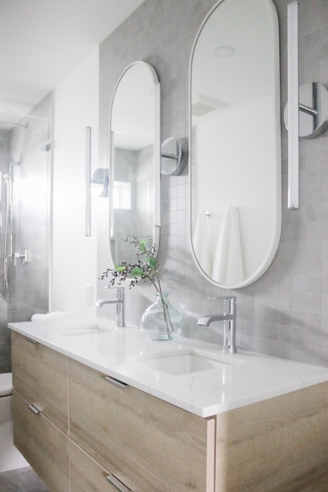 На фото: маленькая главная ванная комната в стиле модернизм с плоскими фасадами, светлыми деревянными фасадами, душем без бортиков, унитазом-моноблоком, серой плиткой, керамической плиткой, белыми стенами, полом из керамогранита, врезной раковиной, столешницей из искусственного кварца, серым полом, открытым душем, белой столешницей, нишей, тумбой под две раковины и подвесной тумбой для на участке и в саду с