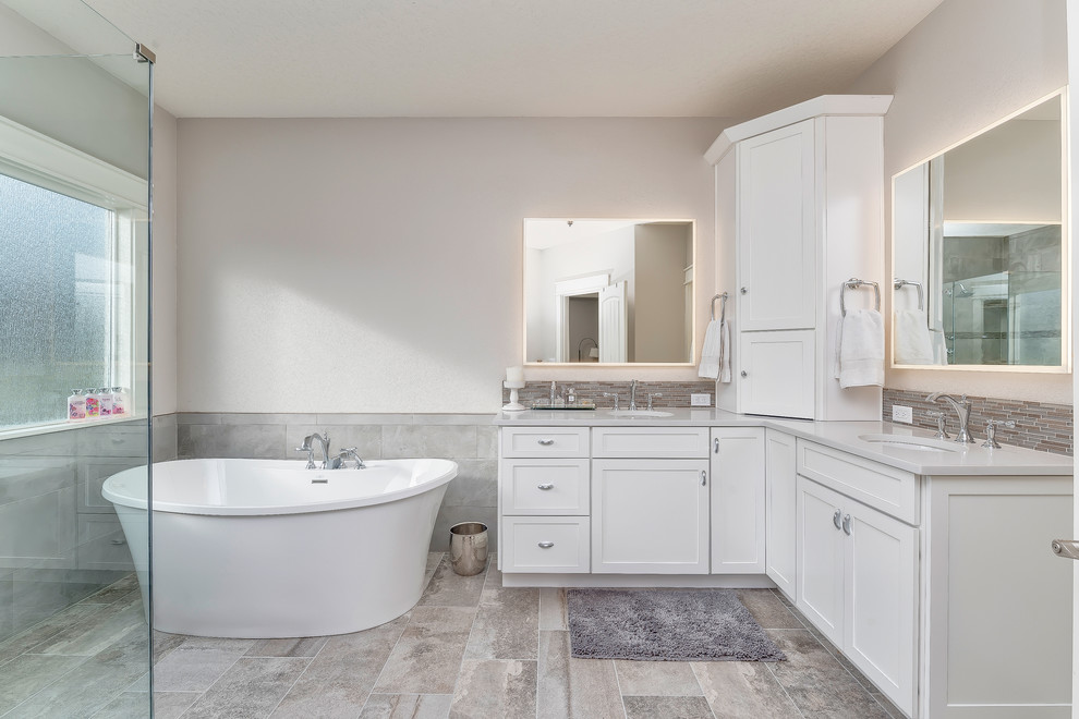 Example of a mid-sized transitional master gray tile and porcelain tile porcelain tile and gray floor freestanding bathtub design in Boise with shaker cabinets, white cabinets, a two-piece toilet, gray walls, an undermount sink, quartz countertops and a hinged shower door
