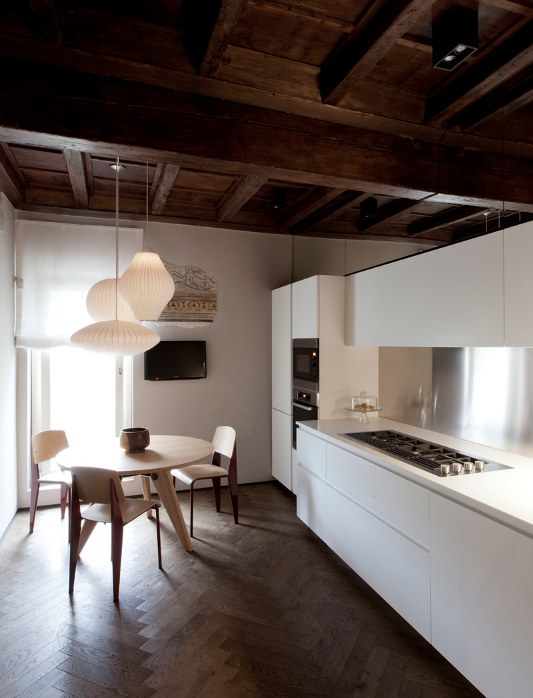 This is an example of a mid-sized contemporary single-wall eat-in kitchen in Milan with flat-panel cabinets, white cabinets, metallic splashback, dark hardwood floors, solid surface benchtops and stainless steel appliances.