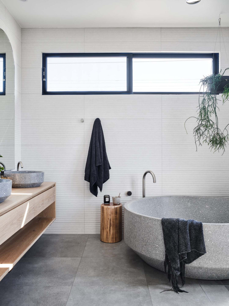 Cette photo montre une salle de bain tendance en bois brun avec un placard à porte plane, une baignoire indépendante, un carrelage blanc, une vasque, un plan de toilette en bois, un sol gris, un plan de toilette marron, meuble double vasque et meuble-lavabo suspendu.
