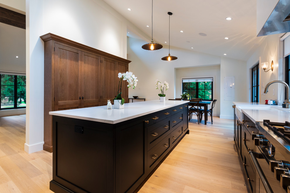 Open concept kitchen - mid-sized rustic l-shaped light wood floor and beige floor open concept kitchen idea in Vancouver with a farmhouse sink, shaker cabinets, black cabinets, quartz countertops, paneled appliances, an island and white countertops