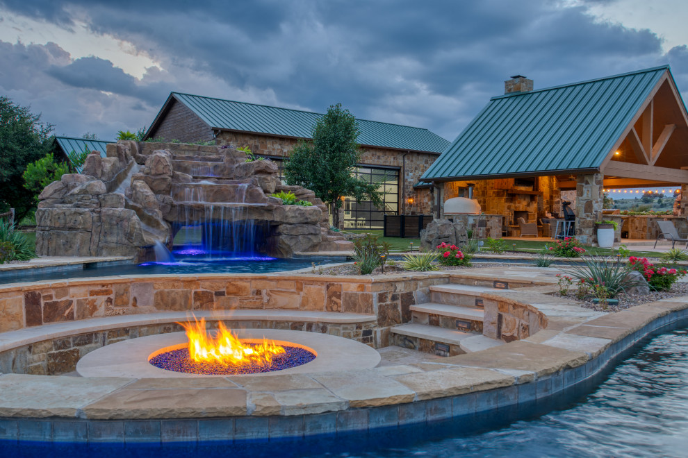This is an example of an expansive country backyard custom-shaped pool in Dallas with a water slide and natural stone pavers.