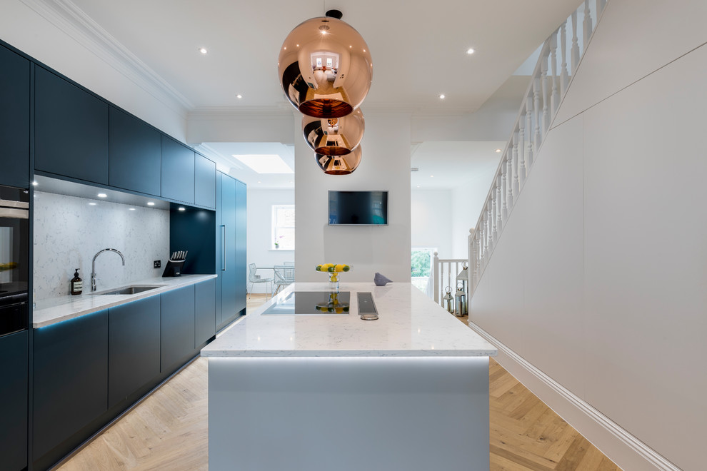 Mid-sized contemporary single-wall open plan kitchen in London with flat-panel cabinets, blue cabinets, quartzite benchtops, stainless steel appliances, with island, white benchtop, white splashback and marble splashback.