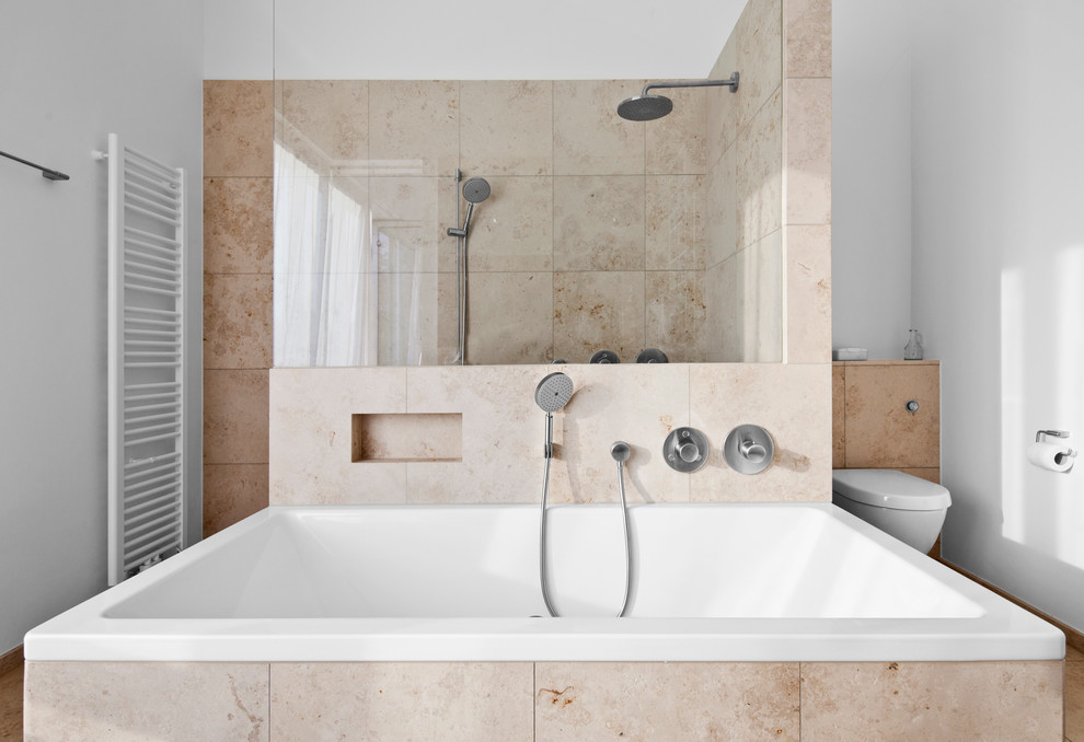 Inspiration for a large contemporary bathroom in Cologne with a drop-in tub, an alcove shower, a wall-mount toilet, beige tile, stone tile, white walls and travertine floors.