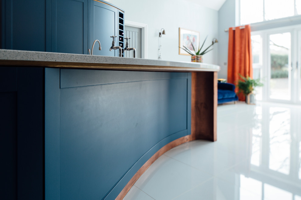 This is an example of a large contemporary l-shaped open plan kitchen in Surrey with a single-bowl sink, shaker cabinets, blue cabinets, quartz worktops, white splashback, stainless steel appliances, porcelain flooring, an island, white floors and white worktops.