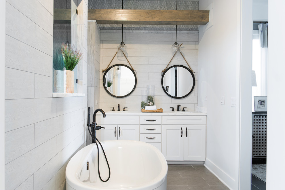 Mid-sized beach style master bathroom in Jacksonville with white cabinets, a freestanding tub, gray tile, ceramic tile, white walls, ceramic floors, marble benchtops, an undermount sink and shaker cabinets.