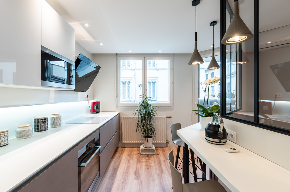 Photo of a mid-sized contemporary l-shaped open plan kitchen in Lyon with an undermount sink, laminate benchtops, white splashback, glass sheet splashback, stainless steel appliances, light hardwood floors, no island and white benchtop.