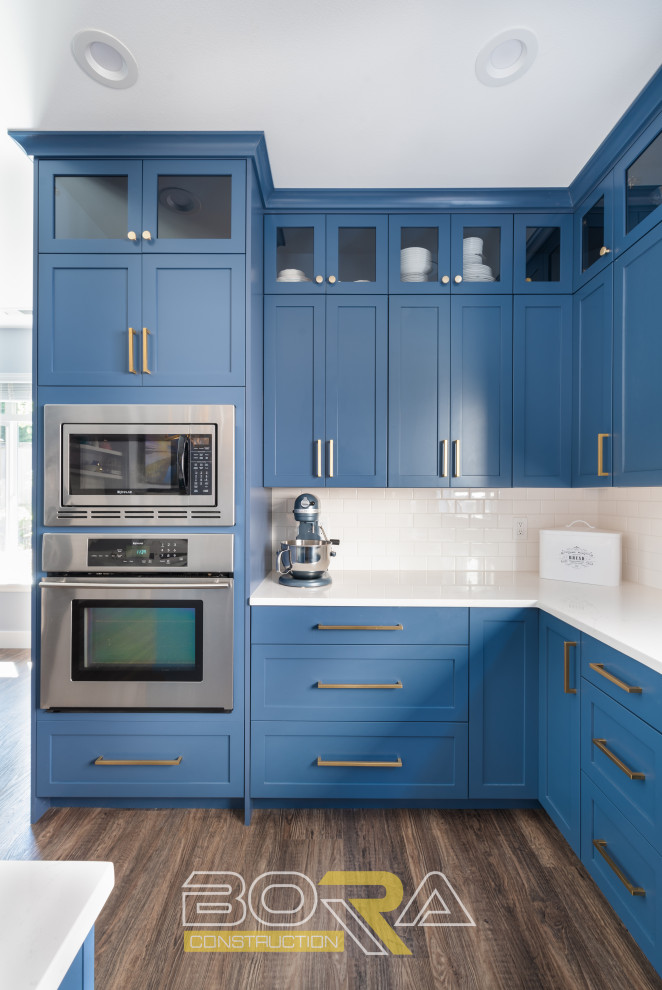 Inspiration for a large l-shaped eat-in kitchen in Seattle with an undermount sink, shaker cabinets, blue cabinets, quartz benchtops, white splashback, ceramic splashback, stainless steel appliances, marble floors, with island, brown floor and white benchtop.