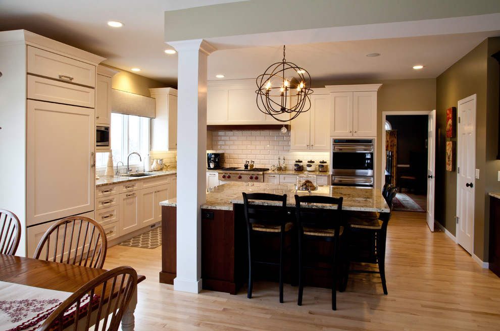 Large transitional l-shaped light wood floor and brown floor open concept kitchen photo with an undermount sink, shaker cabinets, white cabinets, granite countertops, white backsplash, subway tile backsplash, paneled appliances and an island