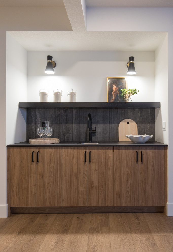 Design ideas for a mid-sized contemporary single-wall wet bar in Calgary with an undermount sink, flat-panel cabinets, light wood cabinets, quartz benchtops, black splashback, porcelain splashback, laminate floors, beige floor and black benchtop.