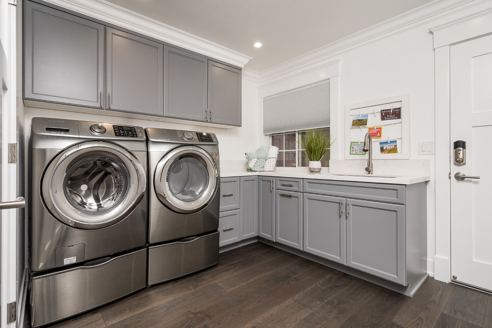 Mid-sized modern l-shaped dedicated laundry room in San Francisco with an undermount sink, shaker cabinets, blue cabinets, quartz benchtops, white walls, laminate floors, a side-by-side washer and dryer and brown floor.