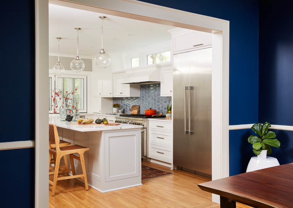 Large transitional kitchen in Minneapolis with a farmhouse sink, recessed-panel cabinets, white cabinets, quartz benchtops, blue splashback, ceramic splashback, stainless steel appliances, light hardwood floors, with island, yellow floor and white benchtop.