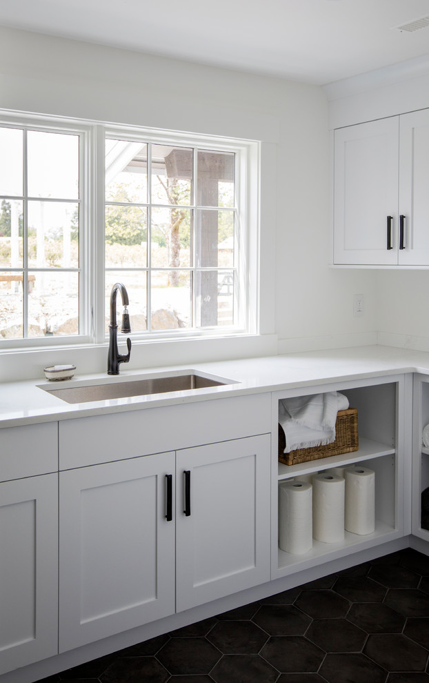 Photo of a country galley dedicated laundry room in Other with shaker cabinets, white cabinets, marble benchtops, white walls, terra-cotta floors, a stacked washer and dryer, black floor and an undermount sink.