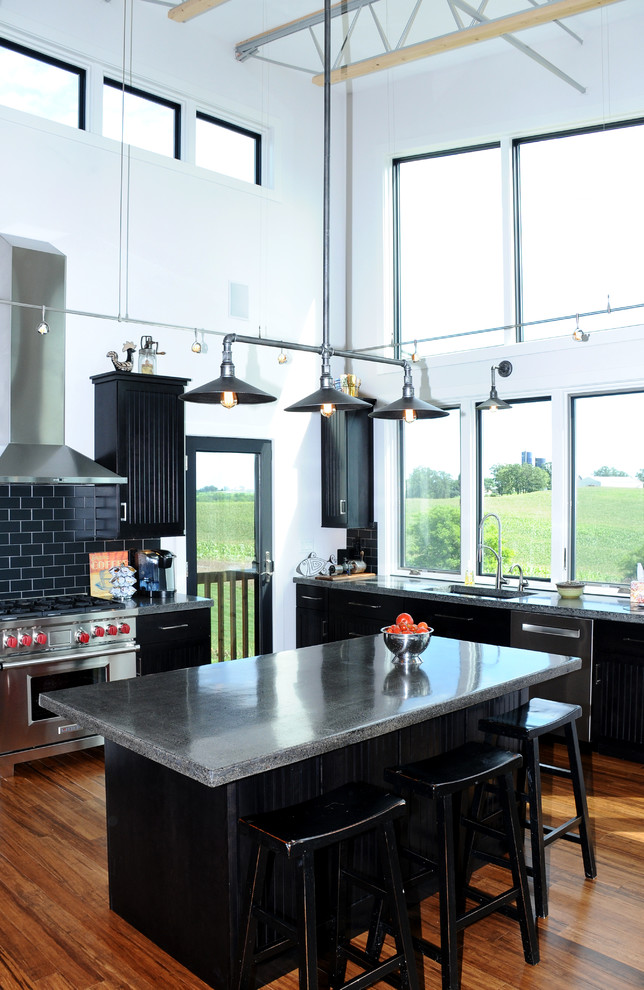 Photo of a mid-sized industrial single-wall open plan kitchen in Other with black cabinets, black splashback, stainless steel appliances, medium hardwood floors, with island, an integrated sink, recessed-panel cabinets, concrete benchtops and ceramic splashback.