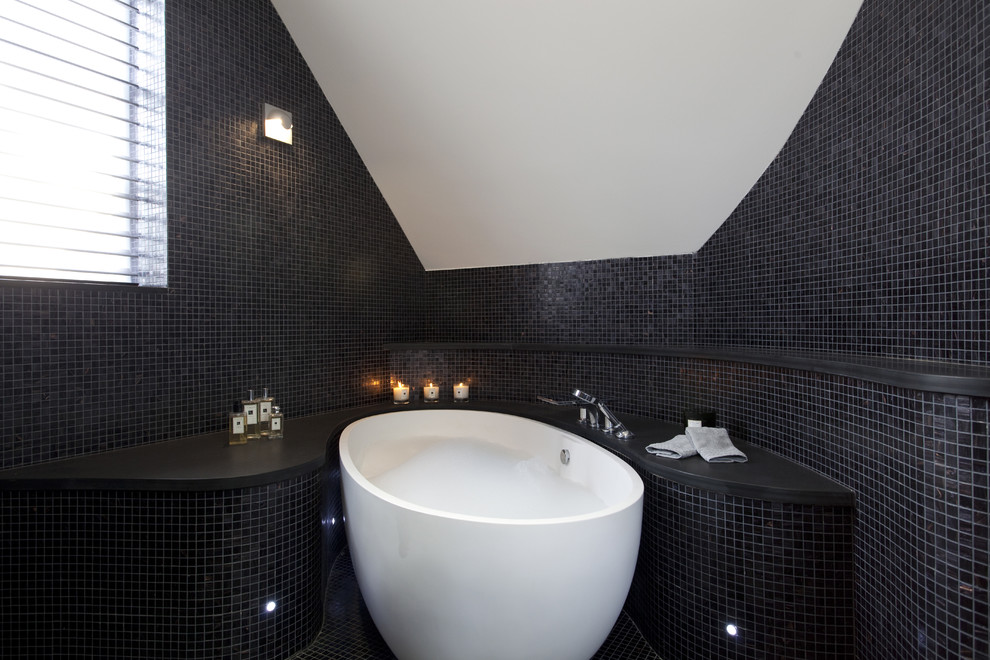 This is an example of a contemporary bathroom in London with a freestanding tub, mosaic tile, black tile and black walls.