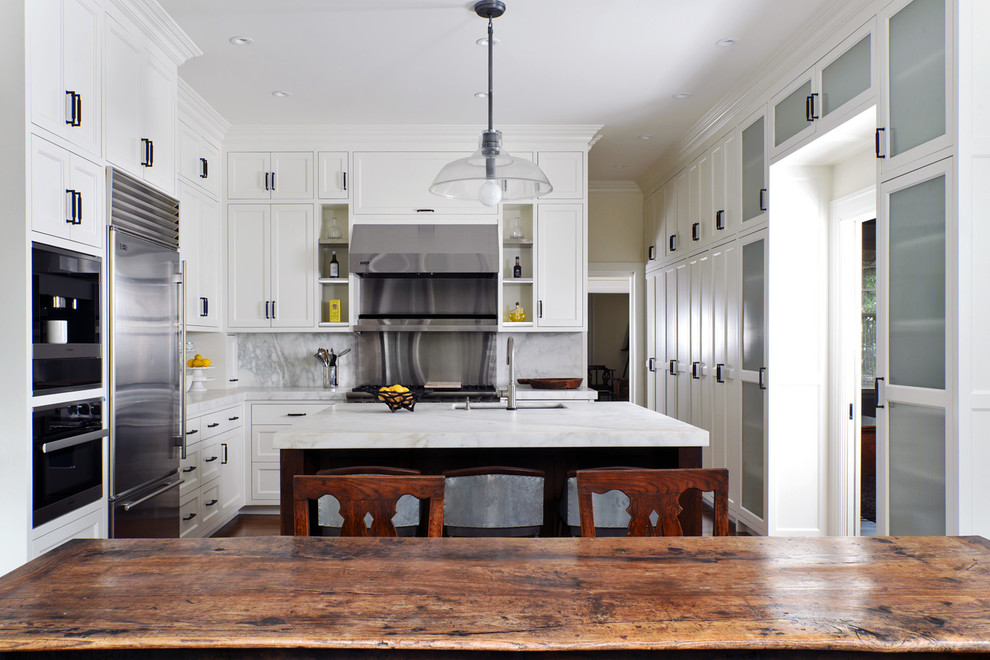 This is an example of a mid-sized transitional u-shaped eat-in kitchen in San Francisco with an undermount sink, recessed-panel cabinets, white cabinets, marble benchtops, white splashback, marble splashback, stainless steel appliances, dark hardwood floors, with island and brown floor.