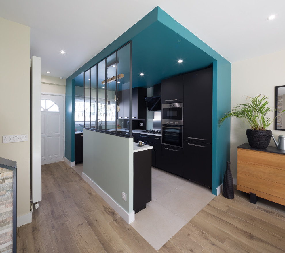 Mid-sized contemporary u-shaped open plan kitchen in Paris with a drop-in sink, flat-panel cabinets, black cabinets, laminate benchtops, black splashback, metal splashback, stainless steel appliances, ceramic floors, with island, beige floor, white benchtop and recessed.