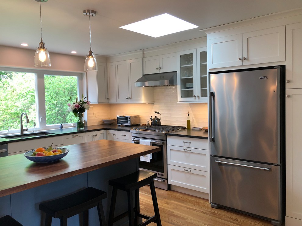 Inspiration for a mid-sized transitional l-shaped medium tone wood floor and brown floor open concept kitchen remodel in Boston with a single-bowl sink, shaker cabinets, white cabinets, granite countertops, white backsplash, window backsplash, stainless steel appliances, an island and black countertops